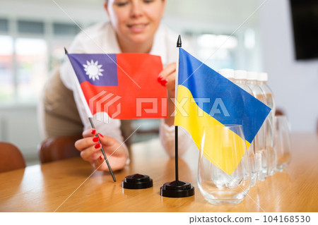 Woman setting flags of Ukraine and Taiwan on negotiating table 104168530