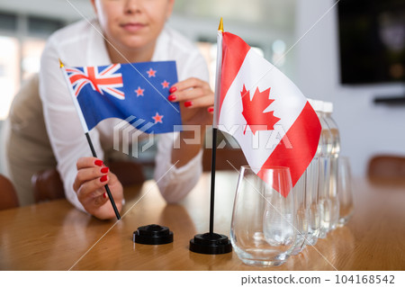 Young woman putting New Zealand and Canada flags on table in office 104168542