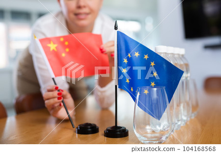 Young woman puts China and EU flags on table in office Young woman puts China and EU flags on table in office 104168568