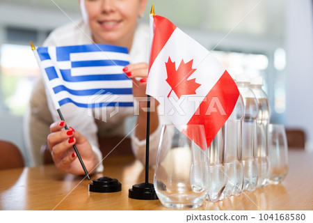 Young woman puts flags of Greece and Canada on table in office Young woman puts flags of Greece and Canada on table in office 104168580