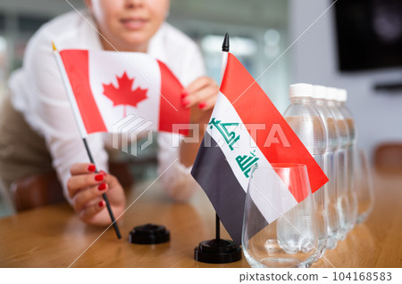 Employee of delegation prepares negotiating table - sets up flag of Canada and Iraq Employee of delegation prepares negotiating table - sets up flag of Canada and Iraq 104168583