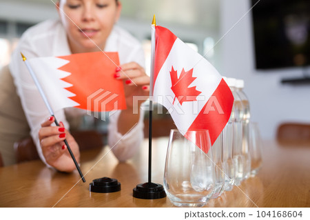 Little flag of Canada on table and flag of Bahrain put next to it by young woman 104168604