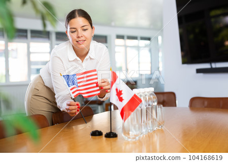 Positive young woman putting little flag of the USA on table next to the flag of Canada Positive young woman putting little flag of the USA on table next to the flag of Canada 104168619