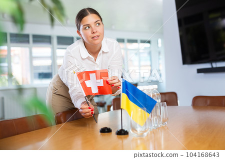 Woman placing flags of Ukraine and Switzerland on negotiating table Woman placing flags of Ukraine and Switzerland on negotiating table 104168643