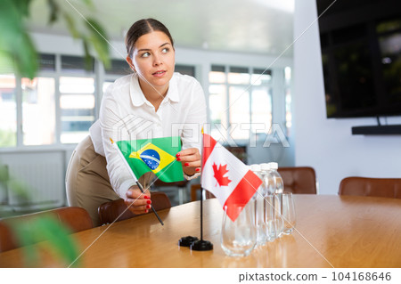 Positive young woman putting little flag of Brazil on table next to the flag of Canada Positive young woman putting little flag of Brazil on table next to the flag of Canada 104168646