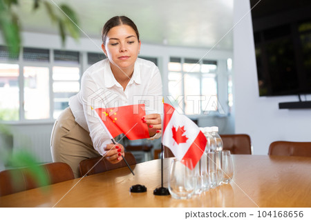 Young woman putting flags of China and Canada on table in office 104168656