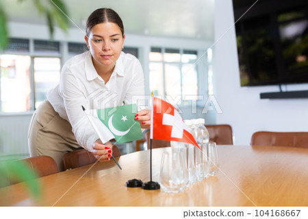 Positive young woman putting little flag of Pakistan on table next to the flag of Switzerland 104168667