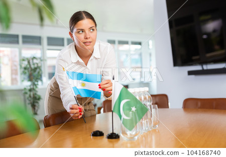 Positive young woman putting little flag of Argentina on table next to the flag of Pakistan 104168740