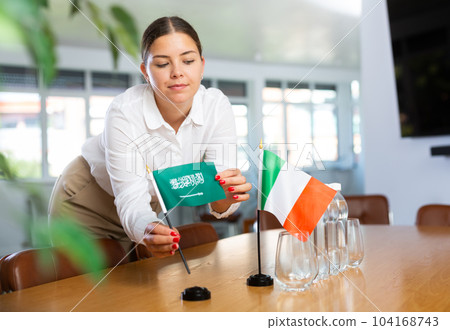 Young woman putting Saudi Arabia and Italy flags on table in office 104168743
