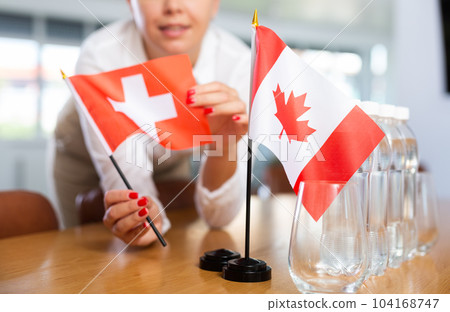 Little flag of Canada on table and flag of Switzerland put next to it by young woman 104168747