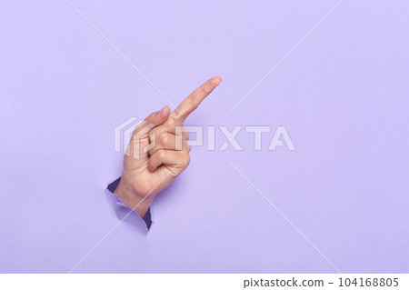 Person's hand breaking through lilac paper wall demonstrates copy space for your promotional content or discount. Advertisement and proposal. Background texture. Banner for sales. 104168805