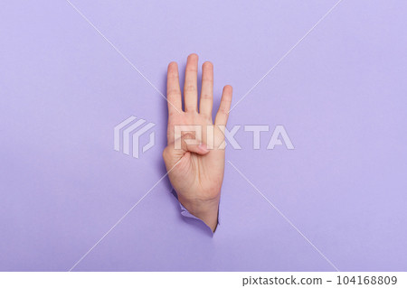 Person's hand sticks out of hole in paper of lilac background four fingers sign, copy space for advertisement. Person's hand sticks out of hole in paper of lilac background four fingers sign, copy space for advertisement. 104168809