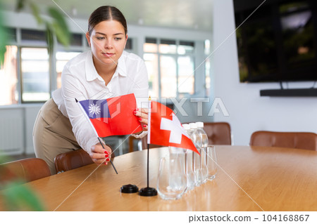 Positive young woman putting little flag of Taiwan on table next to the flag of Switzerland 104168867