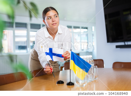 Young lady sets miniatures flags of Ukraine and Finland for international negotiations 104168940