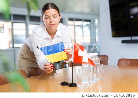 Positive young woman putting little flag of Ukraine on table next to the flag of Switzerland 104168989