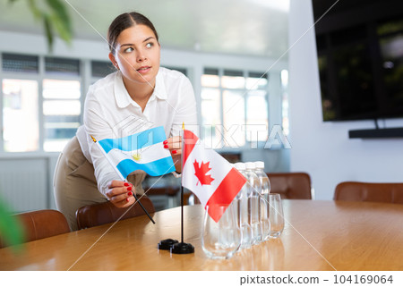 Young woman putting flags of Argentina and Canada on table in office Young woman putting flags of Argentina and Canada on table in office 104169064