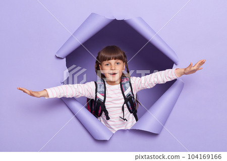 Portrait of happy cute little girl with pigtails wearing striped shirt with backpack raised arms pretending she is flying, raised arms and looking at camera. Portrait of happy cute little girl with pigtails wearing striped shirt with backpack raised arms pretending she is flying, raised arms and looking at camera. 104169166