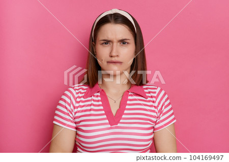 Portrait of scared nervous young Caucasian woman wearing striped T-shirt and hair band posing isolated over pink background, looking at camera and biting lips. Portrait of scared nervous young Caucasian woman wearing striped T-shirt and hair band posing isolated over pink background, looking at camera and biting lips. 104169497