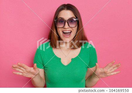Indoor shot of excited astonished amazed woman wearing green t shirt posing isolated over green background, being positive surprised, standing with raised arms and open mouth. 104169550
