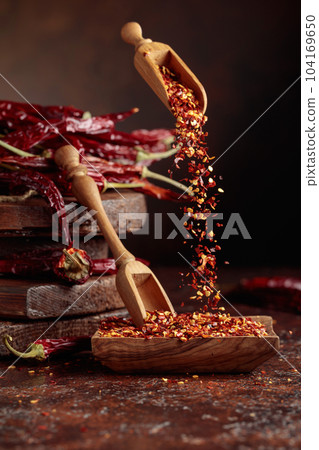 Chilli flakes are poured into a wooden dish. Chilli flakes are poured into a wooden dish. 104169650