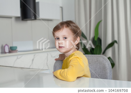 Happy child boy with brown hair in yellow sweater sitting sideways on studio kitchen background Happy child boy with brown hair in yellow sweater sitting sideways on studio kitchen background 104169708