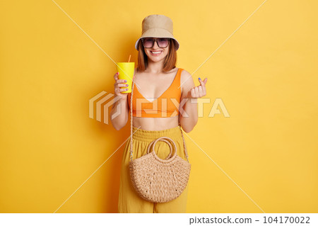 Image of lovely good looking woman in sunglasses wearing summer clothing posing isolated over yellow background, enjoying juice and showing korean love symbol. Image of lovely good looking woman in sunglasses wearing summer clothing posing isolated over yellow background, enjoying juice and showing korean love symbol. 104170022