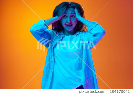 Porrait of young woman hioldingands on head against gradient orange studio background in neon light. Forget task Porrait of young woman hioldingands on head against gradient orange studio background in neon light. Forget task 104170041