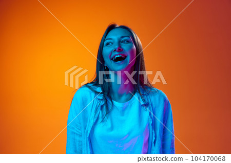 Portrait of beautiful young woman in casual clothes cheerfully laughing, smiling against gradient orange studio background in neon light 104170068