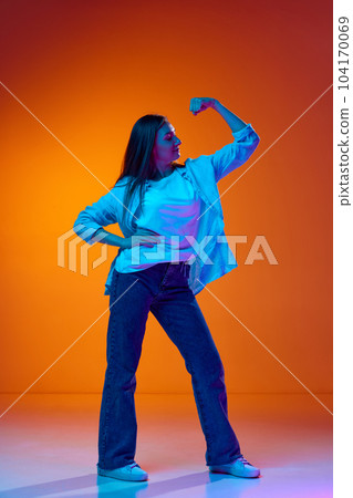 Full-length portrait of young pretty woman in casual clothes posing against gradient orange studio background in neon light 104170069