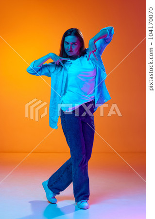 Full-length portrait of young pretty woman in casual clothes posing against gradient orange studio background in neon light 104170070