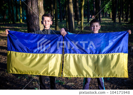 flags of Ukraine in hands of two boys. Children hold Ukrainian flags yellow and blue waving in wind . Ukraine's Independence Day. Flag Day 104171948