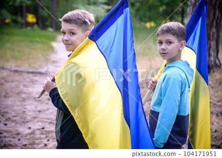 flags of Ukraine in hands of two boys. Children hold Ukrainian flags yellow and blue waving in wind . Ukraine's Independence Day. Flag Day flags of Ukraine in hands of two boys. Children hold Ukrainian flags yellow and blue waving in wind . Ukraine's Independence Day. Flag Day 104171951