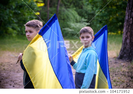 flags of Ukraine in hands of two boys. Children hold Ukrainian flags yellow and blue waving in wind . Ukraine's Independence Day. Flag Day 104171952