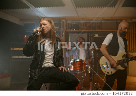 Closed performance of rock band shot with focus on young singer with microphone Closed performance of rock band shot with focus on young singer with microphone 104172052