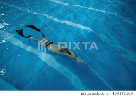 Senior man wearing goggles, cap and flippers swimming in indoor pool Senior man wearing goggles, cap and flippers swimming in indoor pool 104172109