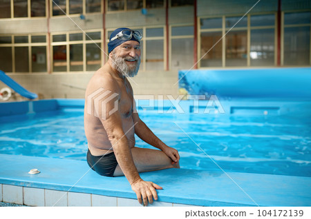 Relaxed senior man in swimming hat and goggles on head sitting at poolside Relaxed senior man in swimming hat and goggles on head sitting at poolside 104172139