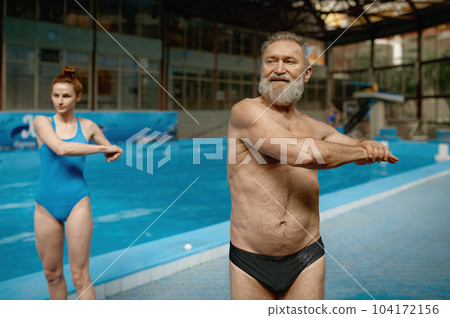 Young woman instructor exercising retired man before training in swimming pool 104172156