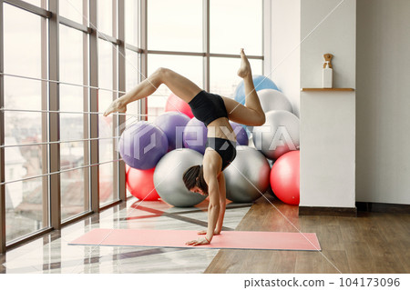 Fitness girl working out at gym with big window. Girl wearing black leggins and sport top. Young woman standing on hands. Fitness girl working out at gym with big window. Girl wearing black leggins and sport top. Young woman standing on hands. 104173096