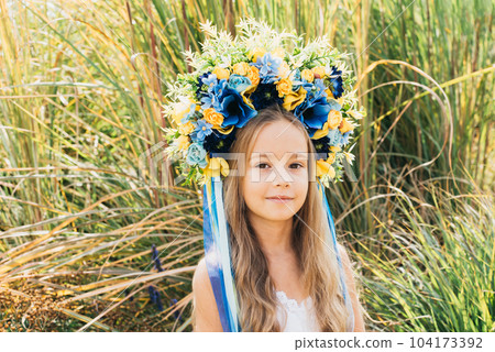 Girl in traditional ukrainian wreath on head blue and yellow flag of Ukraine in field. Ukraine's Independence Flag Day. Constitution day. 24 August. Patriotic holiday. Girl in traditional ukrainian wreath on head blue and yellow flag of Ukraine in field. Ukraine's Independence Flag Day. Constitution day. 24 August. Patriotic holiday. 104173392