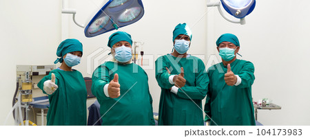 Group of doctor and nurse in surgical green gown uniform stand confidently with finger thumb up before performing an operation in the operating room. Group of doctor and nurse in surgical green gown uniform stand confidently with finger thumb up before performing an operation in the operating room. 104173983