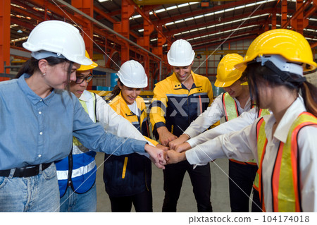 Group of male and female factory labor bumping fist together after finish meeting. Everyone wearing safety uniform and helmet. Workers working in the metal sheet factory. 104174018