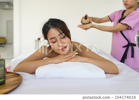 Young asian woman getting spa massage. Lying on a massage table, relaxing with eyes closed.  Spa Thai therapy treatment aromatherapy for beauty body. Spa beauty massage healthy wellness. 104174019