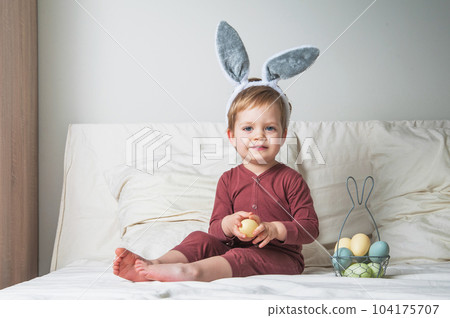 Toddler boy on bed with basket and Easter eggs. Egg hunting, kids activity 104175707