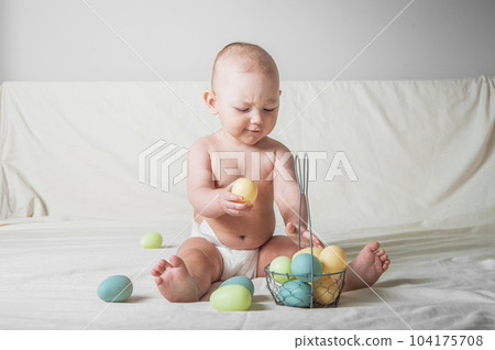 Baby girl 1 year old on bed with basket and Easter eggs. Egg hunting, kids activity Baby girl 1 year old on bed with basket and Easter eggs. Egg hunting, kids activity 104175708