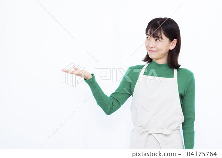 A housewife in her thirties in an apron who is introducing in front of a white background A housewife in her thirties in an apron who is introducing in front of a white background 104175764