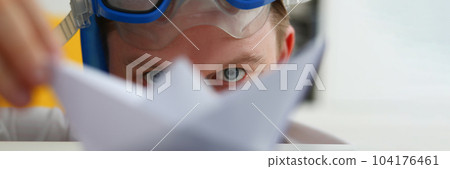 Young man in swimming goggles plays with paper ship at workplace 104176461