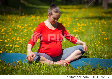 Pregnancy yoga exercise - pregnant woman doing asana baddha konasana bound angle pose outdoors on grass lawn with dandelions in summer 104176507
