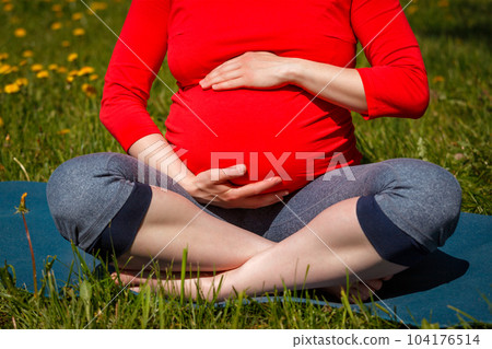 Pregnancy yoga exercise - pregnant woman doing asana Sukhasana easy yoga pose holding her abdomen outdoors on grass lawn with dandelions in summer Pregnancy yoga exercise - pregnant woman doing asana Sukhasana easy yoga pose holding her abdomen outdoors on grass lawn with dandelions in summer 104176514