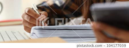 Woman writes hand on agenda while consulting mobile phone on desk at home or in office 104177039