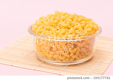 Uncooked Chifferi Rigati Pasta in Glass Jar on Bamboo Mat on Pink Background 104177782